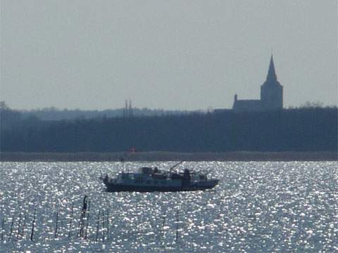 Spiegelndes Achterwasser: Ein Boot fährt vor der Kirche von Lassan entlang.